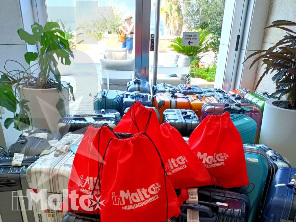 Valigie e zaini rossi personalizzati sono pronti all'ingresso luminoso del resort, tra organizzazione del viaggio e accoglienza a Malta.