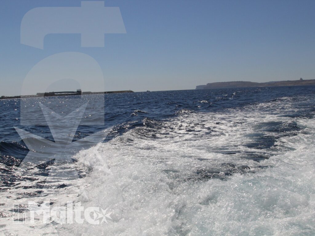 Scia bianca lasciata da una barca in navigazione, con mare aperto e costa bassa all'orizzonte