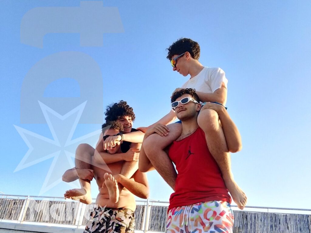 Studenti sulla sabbia durante la giornata a Mellieħa Bay Quattro studenti posano e si muovono sulla sabbia sotto il cielo limpido, condividendo un momento spontaneo a Mellieħa Bay.