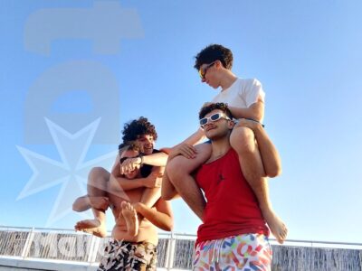 Quattro studenti posano e si muovono sulla sabbia sotto il cielo limpido, condividendo un momento spontaneo a Mellieħa Bay.