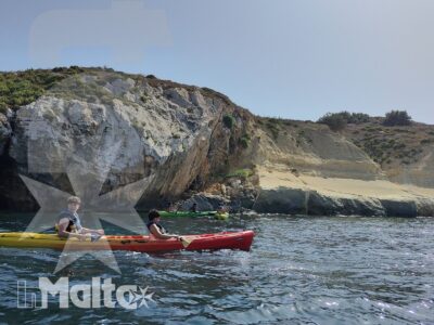 Due studenti remano su kayak colorati davanti alla costa rocciosa di Malta, immersi in un'attività nautica dal mare limpido.