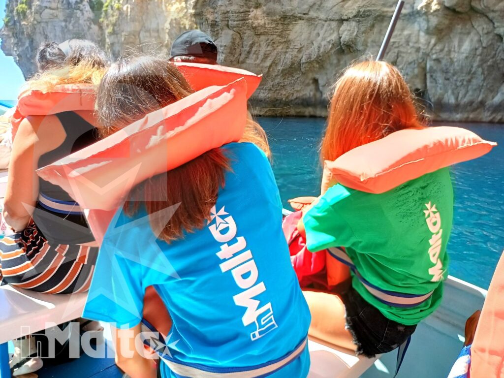 Un gruppo di studenti siede in barca tra acque turchesi e pareti rocciose durante l'escursione marina alla Blue Grotto.