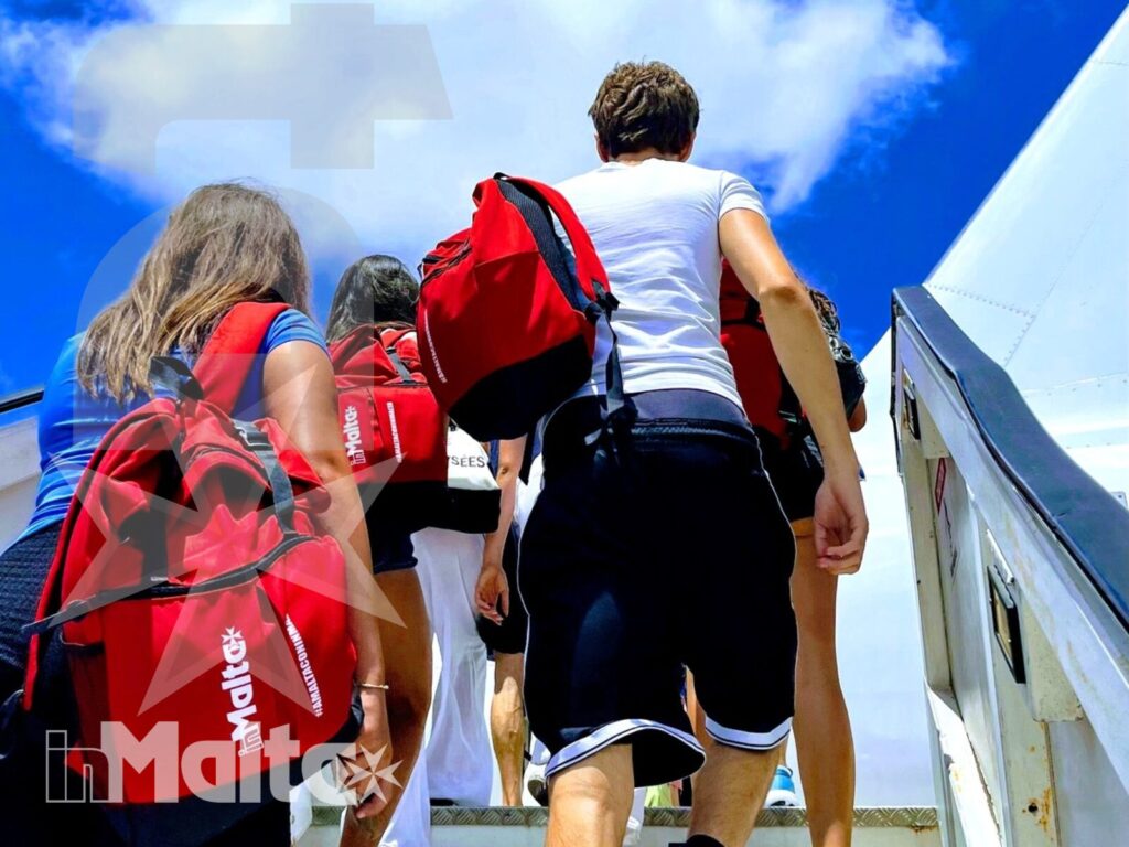 Studenti con zaini rossi salgono la scaletta dell'aereo sotto un cielo limpido, all'inizio del viaggio inMalta.
