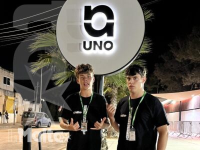 Due studenti sorridono davanti all'insegna luminosa di un locale, mostrando i tesserini durante un'uscita serale a Malta.