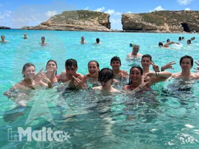 Gruppo di studenti sorride e gioca immerso nell'acqua turchese, con scogliere calcaree sullo sfondo della giornata alla Blue Lagoon.