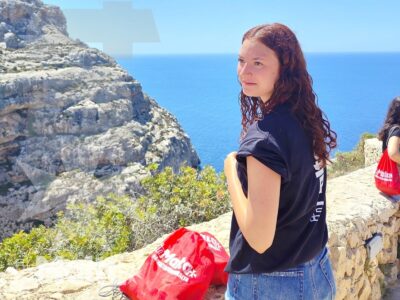 Studentessa con zaino rosso osserva il mare dalla scogliera durante un'escursione panoramica sulla costa di Malta.