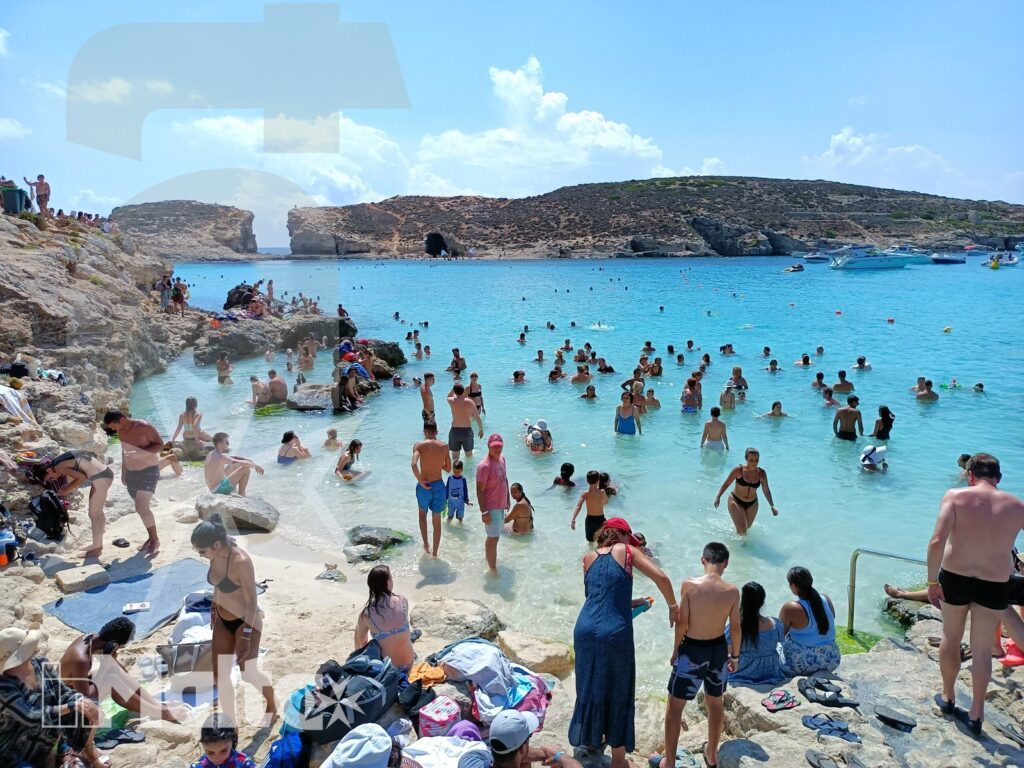 Caletta balneabile affollata sulla costa maltese Caletta maltese affollata di bagnanti, circondata da scogliere e barche in una luminosa giornata estiva.
