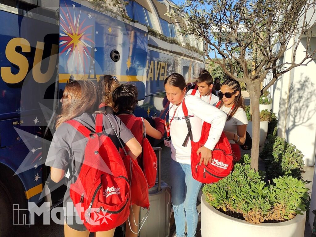 Studenti con zaini coordinati salgono accanto a un pullman turistico, durante un trasferimento organizzato dalla struttura a Malta.