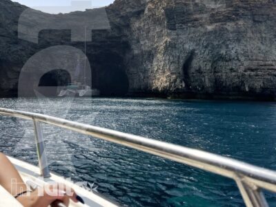 Falesia rocciosa con grotta marina e acqua turchese osservata dal ponte di una barca durante un'escursione a Comino