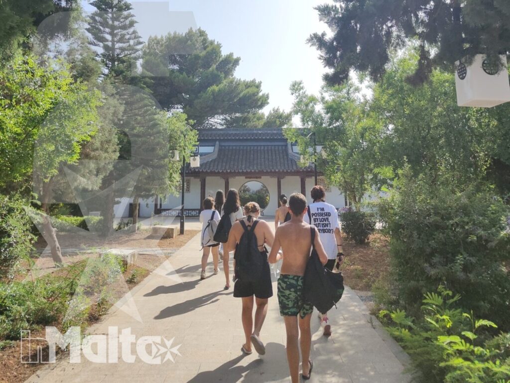 Gruppo di studenti cammina lungo un viale alberato verso un edificio tradizionale durante l'escursione culturale inMalta.