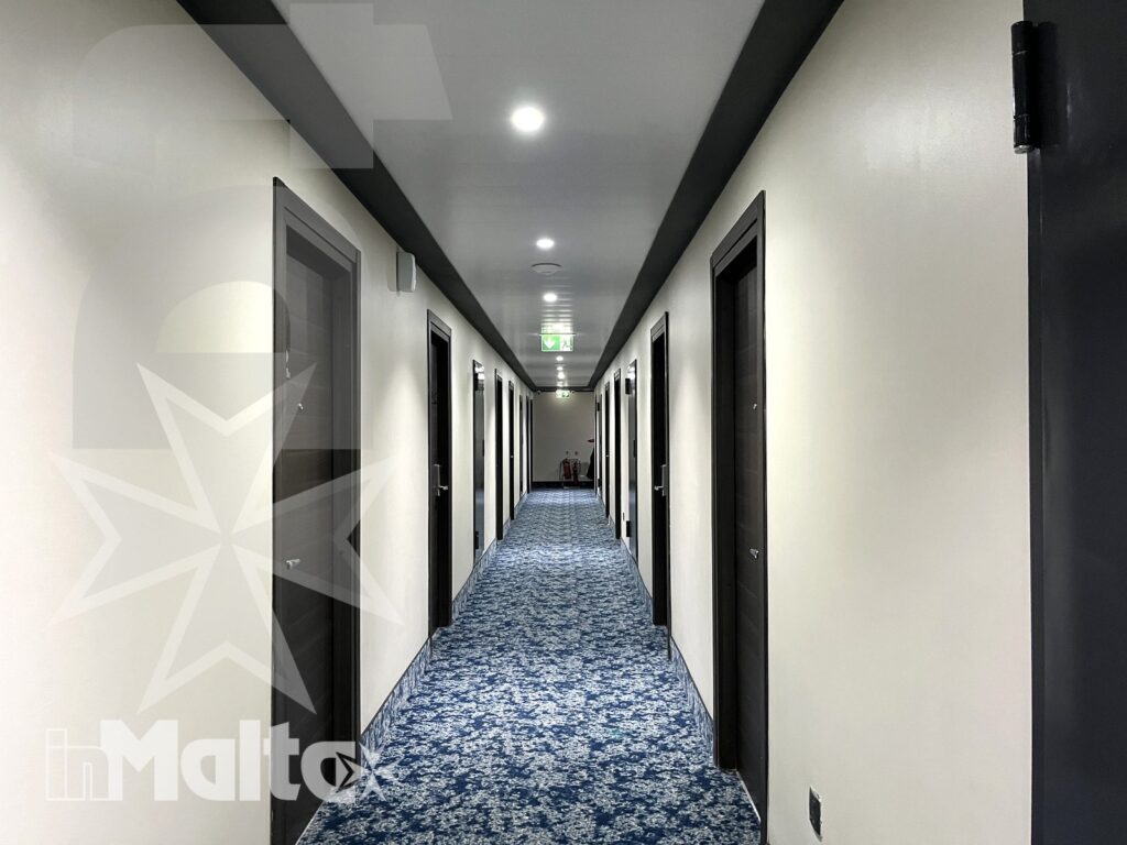 Corridoio moderno e accessi alle camere della struttura ricettiva Corridoio alberghiero lungo e simmetrico, con porte scure, moquette decorata e illuminazione uniforme per l'accesso alle camere.