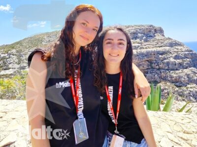 Due studentesse sorridono abbracciate davanti alle rocce e al mare della costa maltese, ritratte durante un'escursione del gruppo.