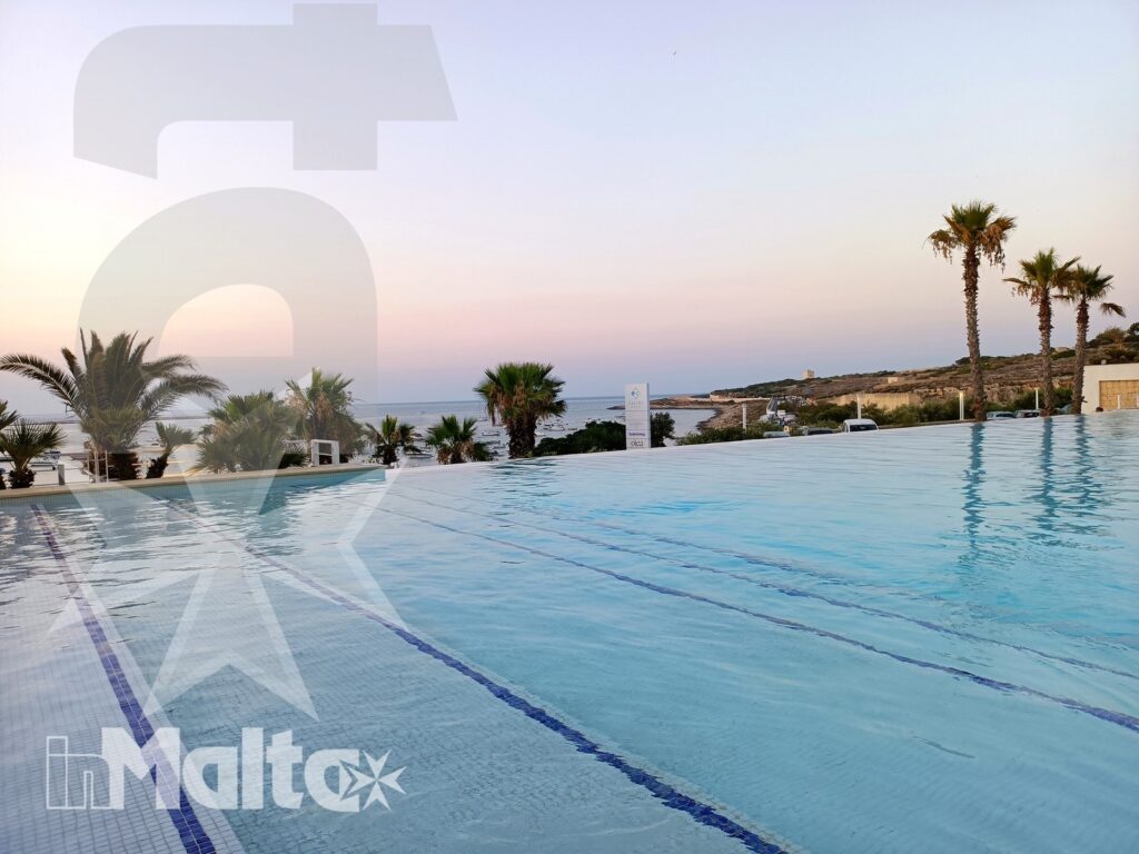 Piscina a sfioro del resort con vista sul mare Piscina a sfioro vuota con palme, vista sul mare e paesaggio costiero mediterraneo.