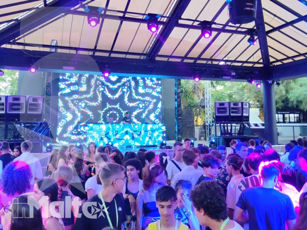 Evento musicale per studenti durante il soggiorno a Malta Studenti si ritrovano in una struttura coperta per un evento musicale, illuminati da luci blu e viola e da un grande schermo LED.