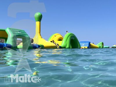 Parco acquatico gonfiabile multicolore sul mare, con scivoli, ostacoli e partecipanti impegnati nei giochi d'acqua.