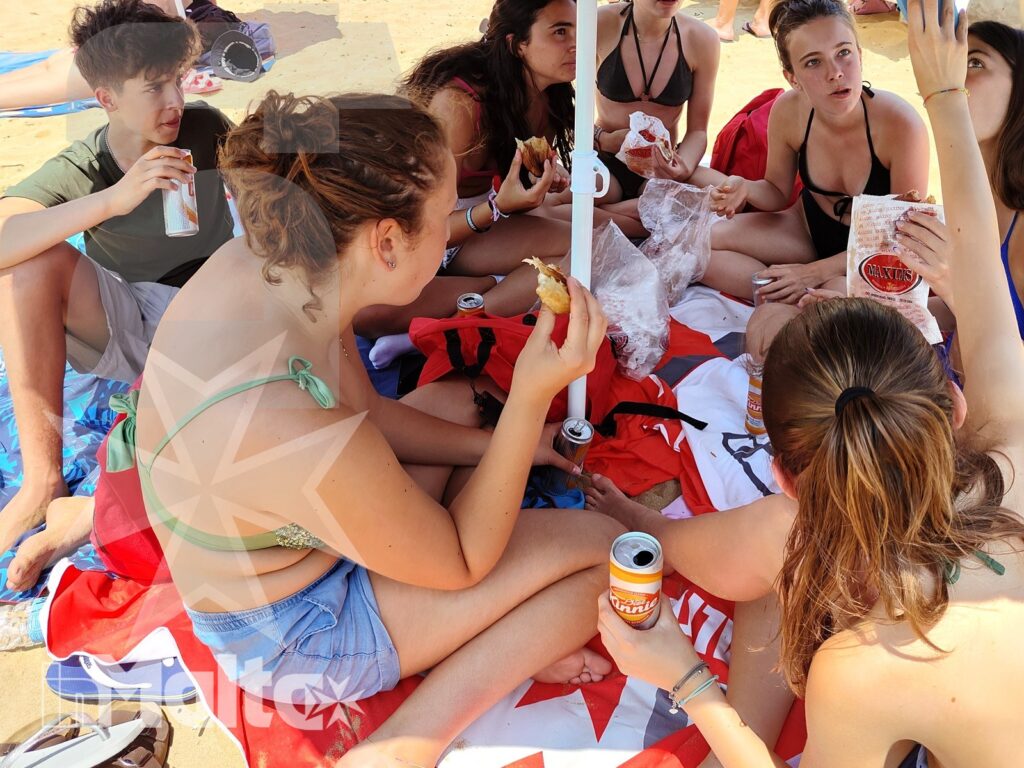 Picnic tra studenti sulla spiaggia di Golden Bay Studenti condividono cibo e bevande su un telo colorato in spiaggia, vivendo un momento di socialità durante il soggiorno studio.