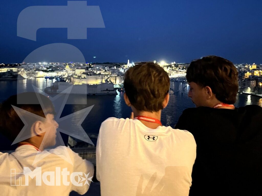 Studenti durante una serata sul porto di Malta Tre studenti osservano di spalle il porto illuminato, con le luci della città riflesse sull'acqua durante la serata.