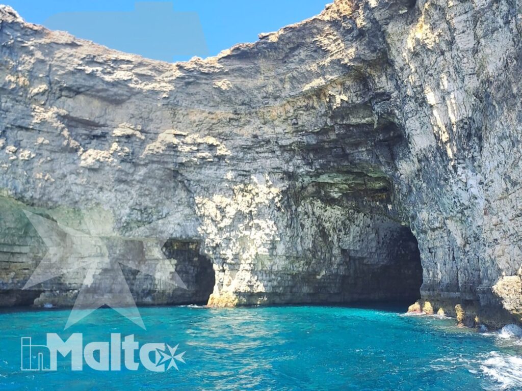 Una grotta marina si apre tra pareti calcaree stratificate e acqua turchese durante la navigazione lungo la costa di Malta.