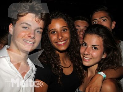 Quattro studenti sorridono ravvicinati durante un momento di socialità serale, con braccialetti identificativi al polso.