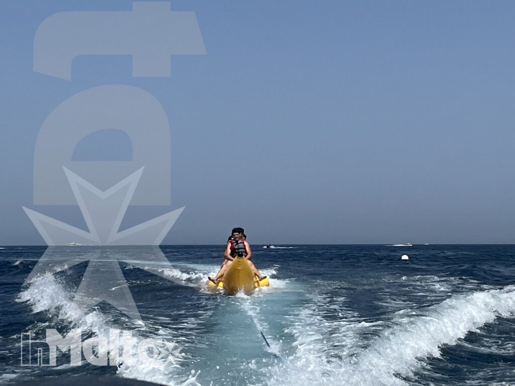 Una persona viene trainata su un gonfiabile giallo tra onde e spruzzi, lasciando una scia bianca sul mare aperto.