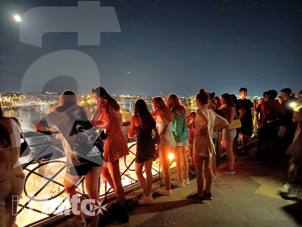 Studenti affacciati a una terrazza panoramica condividono un momento conviviale davanti alla città illuminata durante una vacanza studio.