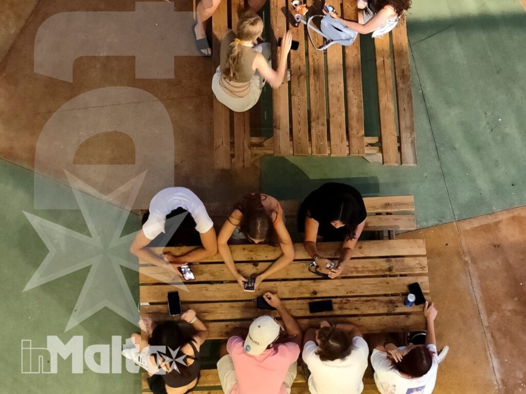 Due gruppi di studenti partecipano insieme a un'attività ai tavoli di legno, osservati dall'alto durante il soggiorno studio.
