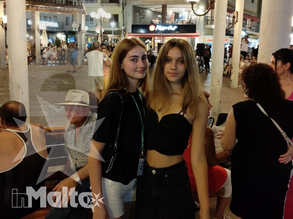 Due studentesse sorridono in una piazza illuminata di sera, circondate da giovani e visitatori durante un soggiorno studio a Malta.