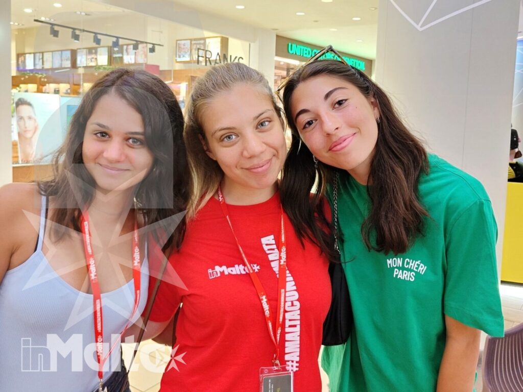 Studentesse inMalta condividono un momento di socialità Tre studentesse sorridono insieme in un ambiente interno, indossando badge identificativi durante il loro soggiorno studio.