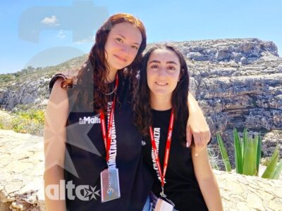 Due studentesse sorridenti e abbracciate posano davanti a una scogliera rocciosa durante un'escursione del gruppo.