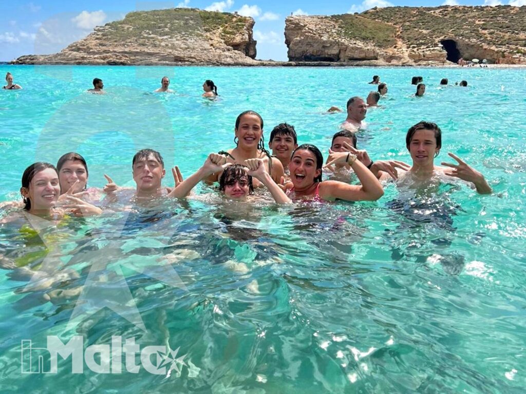 Studenti in acqua alla Blue Lagoon Gruppo di studenti sorride nell'acqua turchese davanti alla costa rocciosa con arco naturale della Blue Lagoon.
