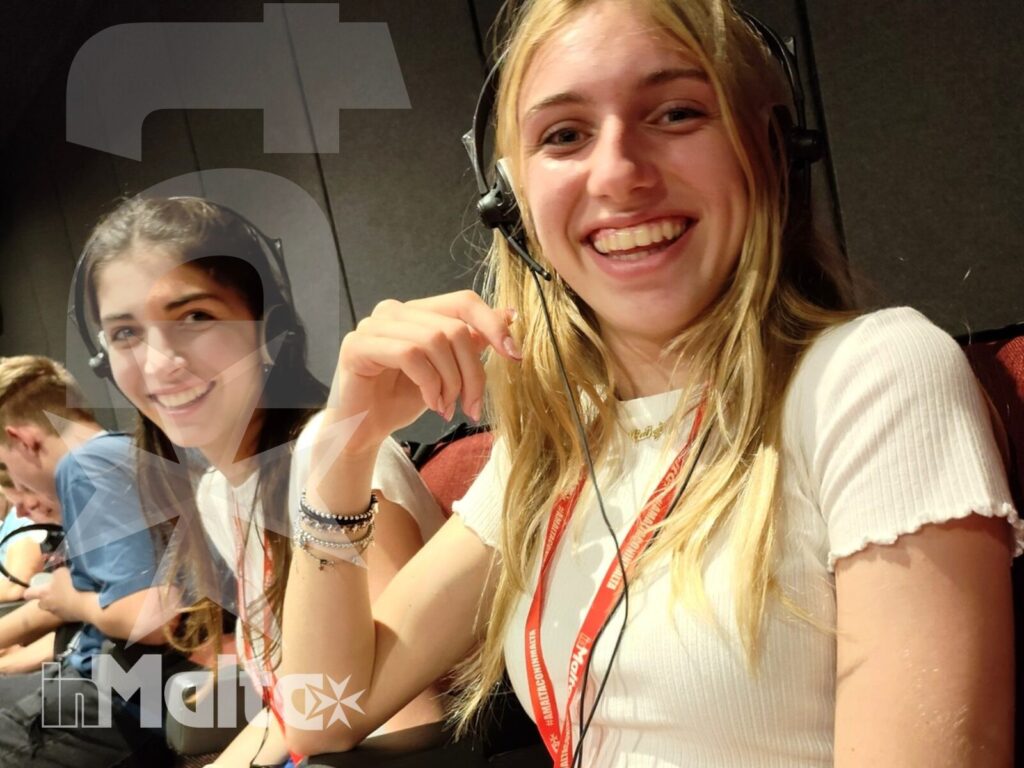 Studentesse durante un'attività del soggiorno linguistico Due studentesse sorridono indossando cuffie e tesserini durante un'attività di gruppo al chiuso, parte del loro soggiorno linguistico.