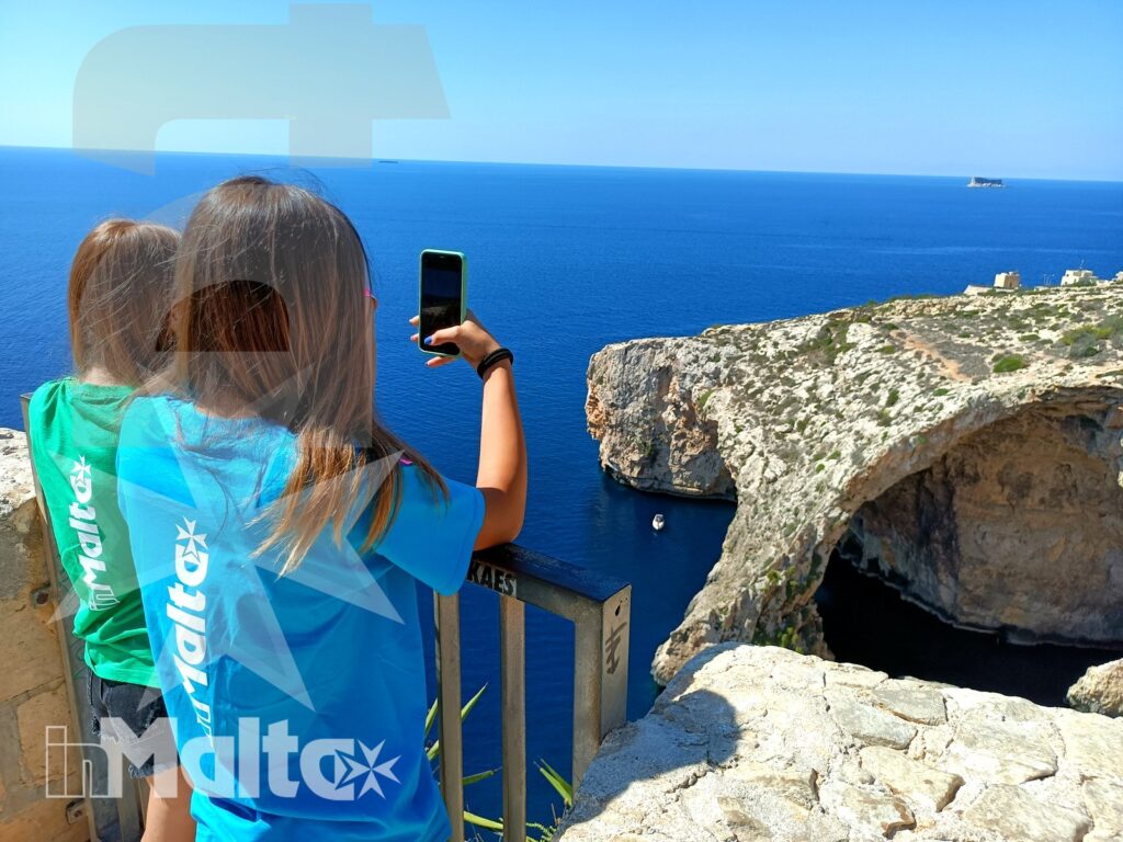 Due studentesse fotografano con lo smartphone la scogliera calcarea durante un'escursione costiera inMalta.