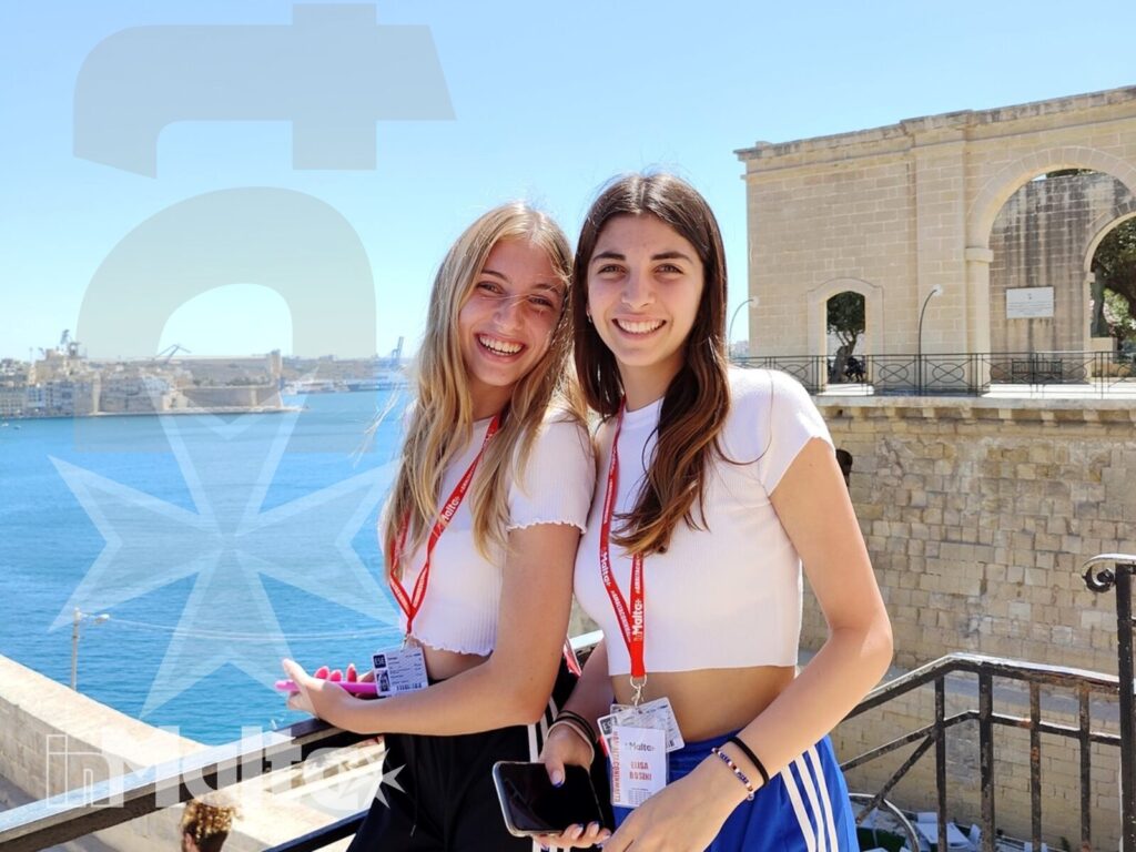 Studentesse durante un soggiorno studio davanti al mare maltese Due studentesse sorridono su una terrazza panoramica, accanto a un edificio storico e con il mare sullo sfondo.