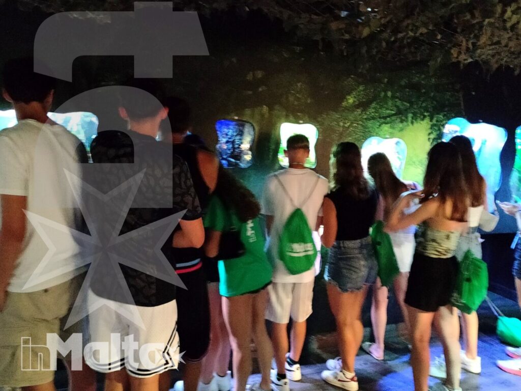 Un gruppo numeroso di studenti osserva vasche e installazioni marine illuminate durante un'attività culturale a Malta.