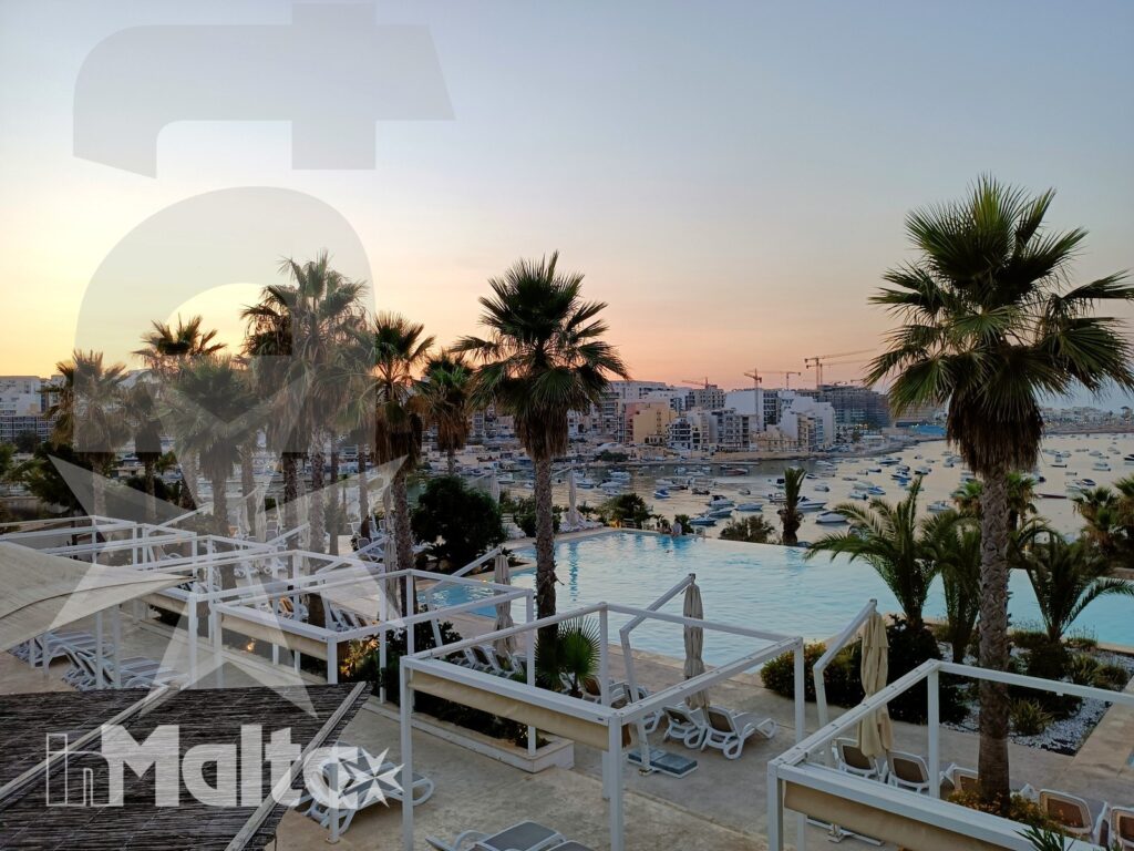 Piscina panoramica con palme, terrazze su più livelli e vista sulla costa durante il tramonto.