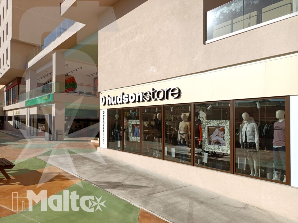 Facciata del negozio Hudsonstore con manichini vestiti, vetrine e pavimentazione colorata in una galleria commerciale all'aperto di Malta.