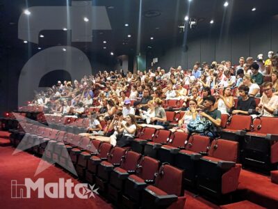 Ampio gruppo di studenti siede sulle poltrone rosse a gradoni di un auditorium durante un'attività collettiva inMalta.