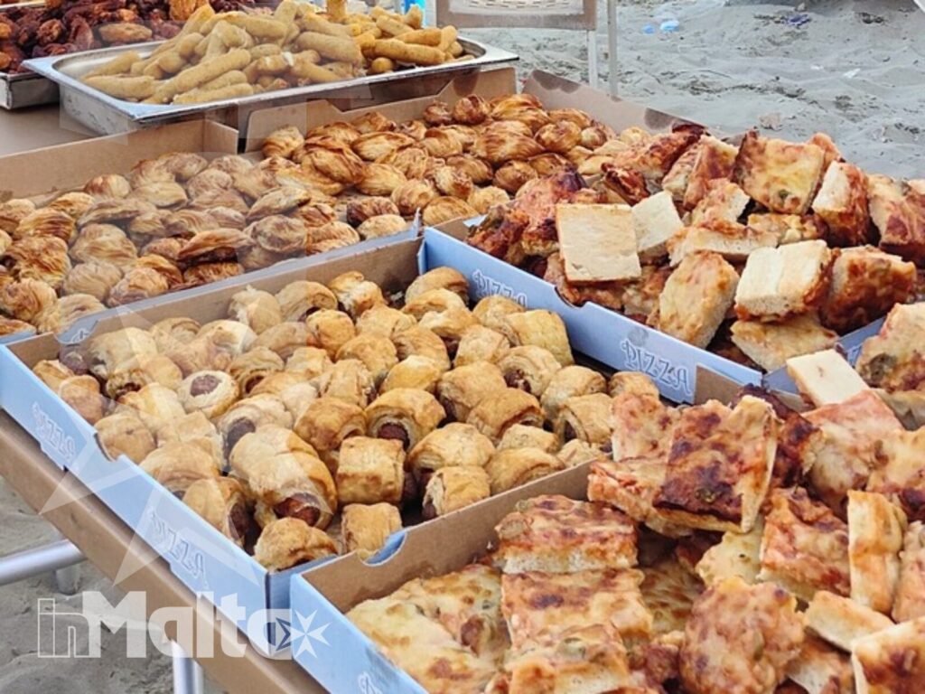 Specialità da forno durante l'escursione a Mellieha Bay Banco all'aperto ricco di specialità da forno, con venditrice e cliente durante un momento gastronomico dell'escursione a Mellieha Bay.
