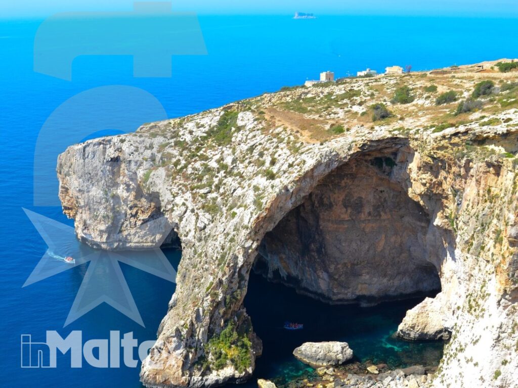 Veduta dall'alto di un arco naturale sulla costa calcarea, con acqua turchese e una piccola grotta affacciata sul Mediterraneo.