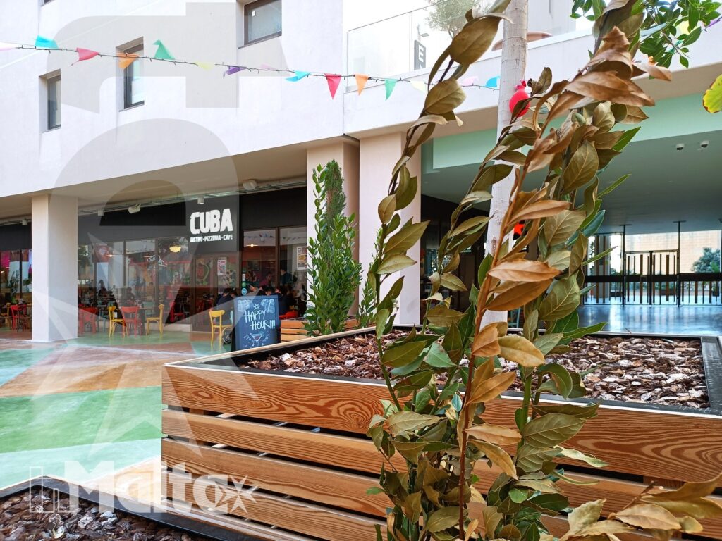Cortile interno del Campus Hub con fioriera in legno, decorazioni a bandierine e negozio CUBAI sullo sfondo.