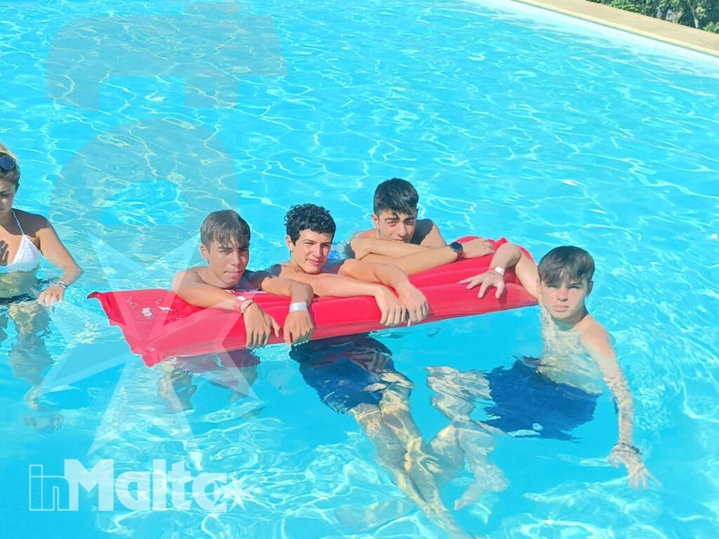 Gruppo di studenti circonda un materassino rosso in piscina durante un momento di svago condiviso.