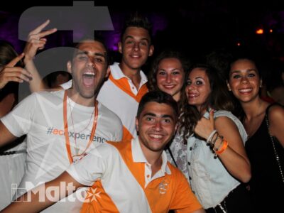 Sei studenti sorridenti posano insieme in discoteca, avvolti dalle luci viola durante una serata internazionale a Malta.