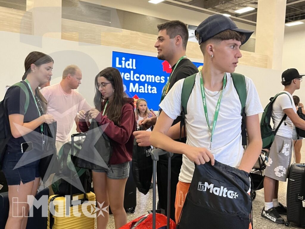 Studenti con valigie colorate e accompagnatori attendono nell'area arrivi dell'aeroporto di Malta durante l'accoglienza del gruppo