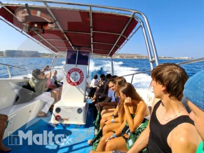 Gruppo di studenti a bordo di un motoscafo con tendalino rosso, in navigazione sul mare di Malta verso la costa.