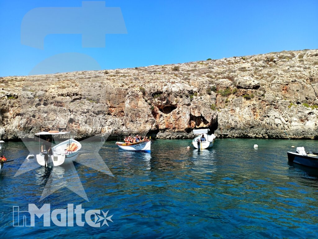 Barche turistiche nella baia della Blue Grotto a Malta Piccole barche da escursione sostano in una baia maltese dalle acque blu, circondata da scogliere calcaree e grotte naturali.