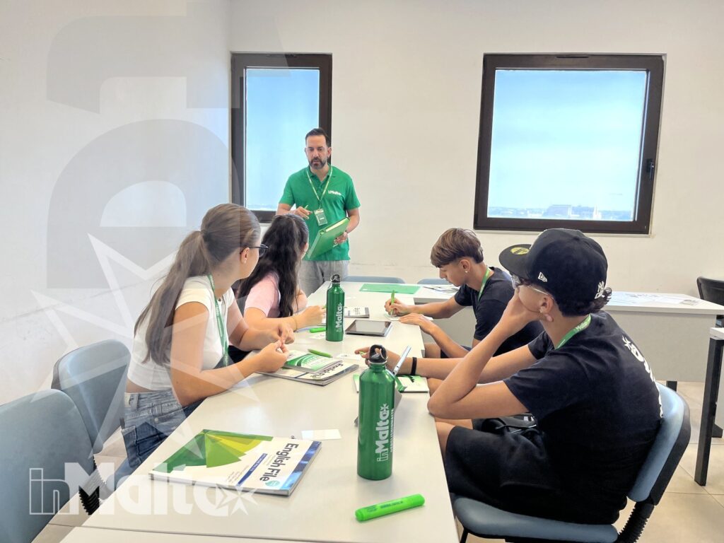 Apprendimento collaborativo degli studenti in aula Studenti lavorano insieme su quaderni e dispense mentre un tutor coordina l'attività, in un'aula luminosa durante il soggiorno formativo.