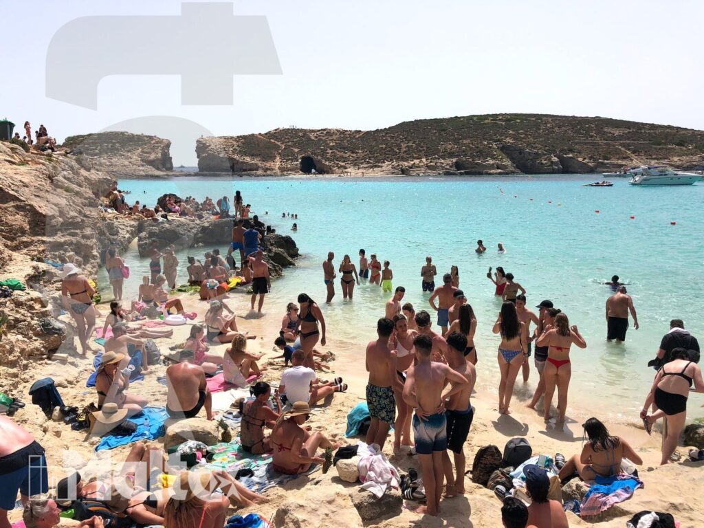 Giornata al mare nella baia turchese di Malta Bagnanti nuotano e si rilassano nella baia turchese, circondata da rocce, barche e attrezzatura da spiaggia.