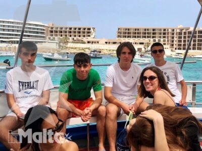 Studenti e accompagnatori condividono una gita a bordo di una barca in un porto turistico maltese dalle acque turchesi.