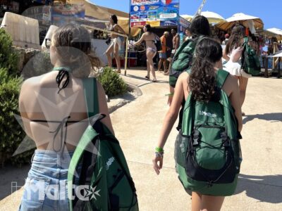 Studentesse con zaini coordinati camminano tra bancarelle e ristoranti di una vivace località maltese, durante una pausa dell'escursione.