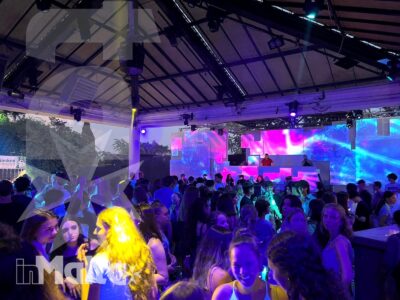 Folla di studenti riunita davanti a un DJ e a schermi luminosi, durante una festa serale in una struttura coperta.